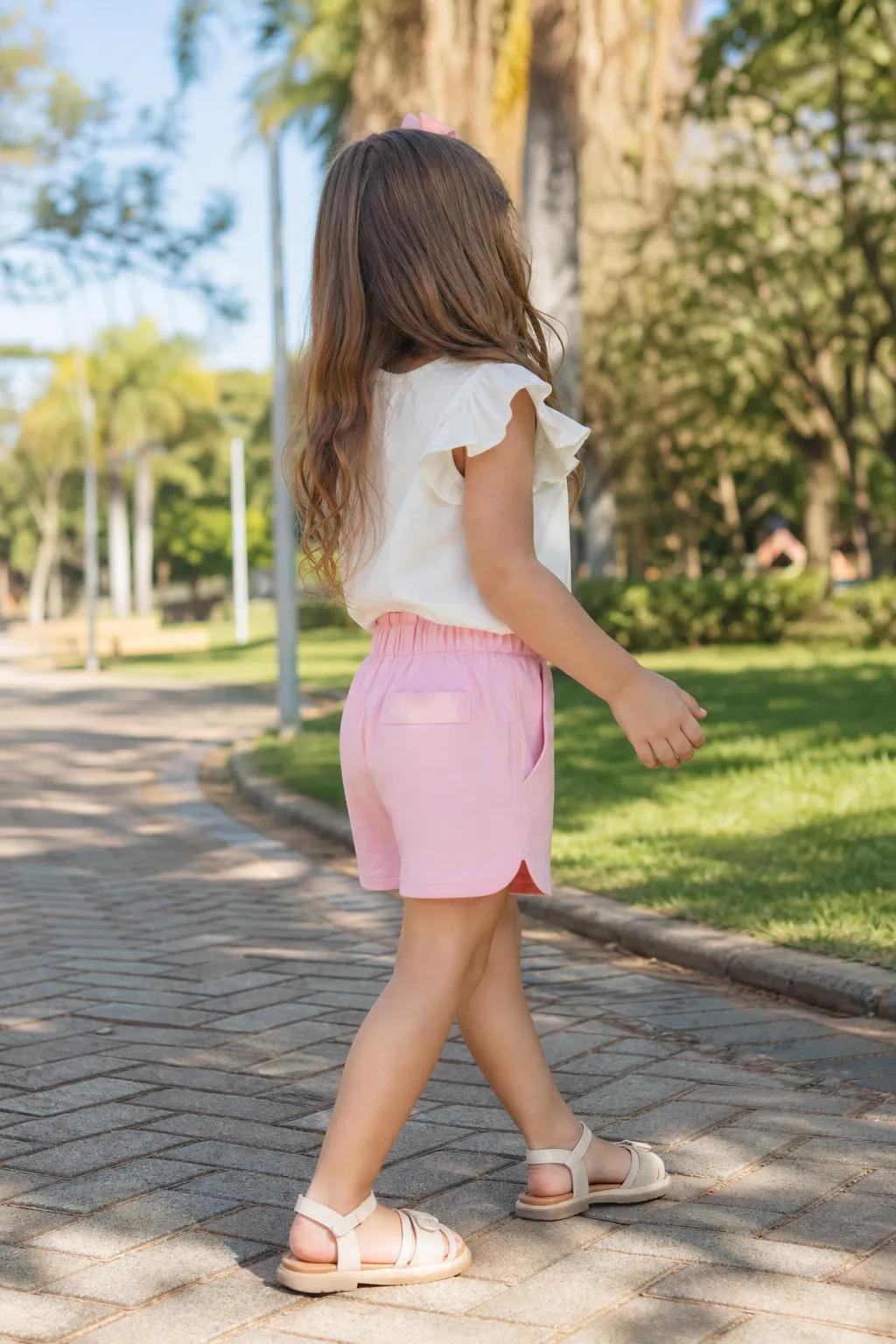 Menina usando conjunto infantil feminino com blusa clara e short rosa em passeio ao ar livre