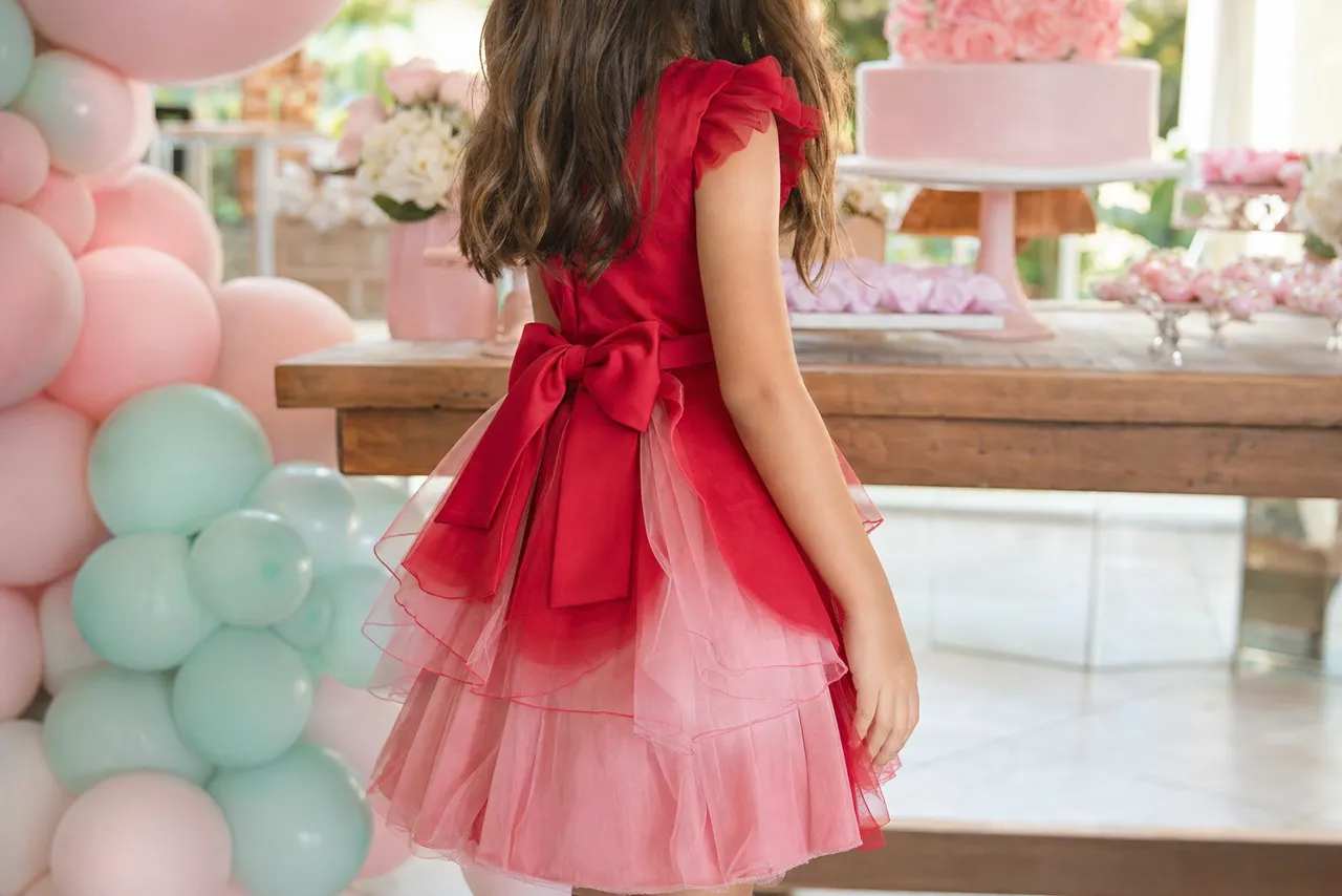 Menina sem rosto identificável usando vestido infantil vermelho e rosa em cenário de aniversário
