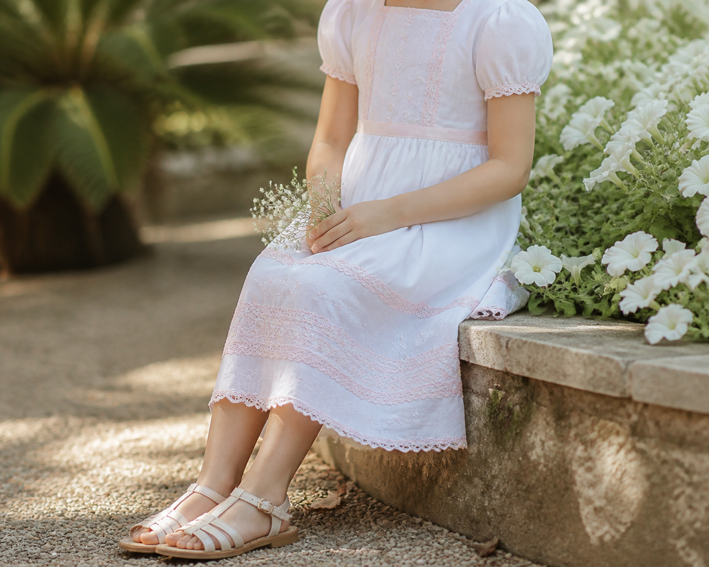 Menina com vestido claro confortável em jardim após cerimônia de batizado